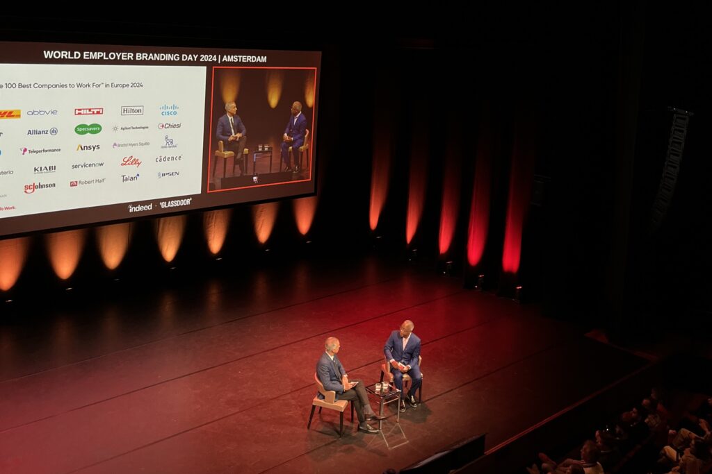 Two men speaking on a stage infront of an audience