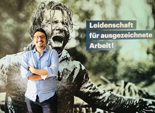 man smiling with crossed arms while standing infront of a poster showcasting another man doing mudsports