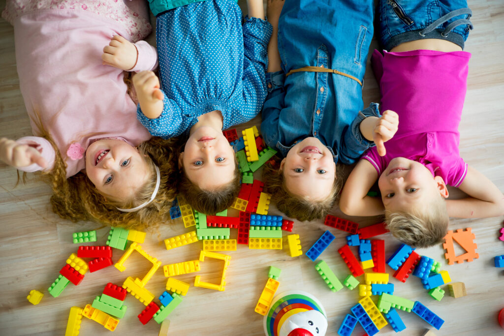 four children lying upside down on the ground next to toy building blocks