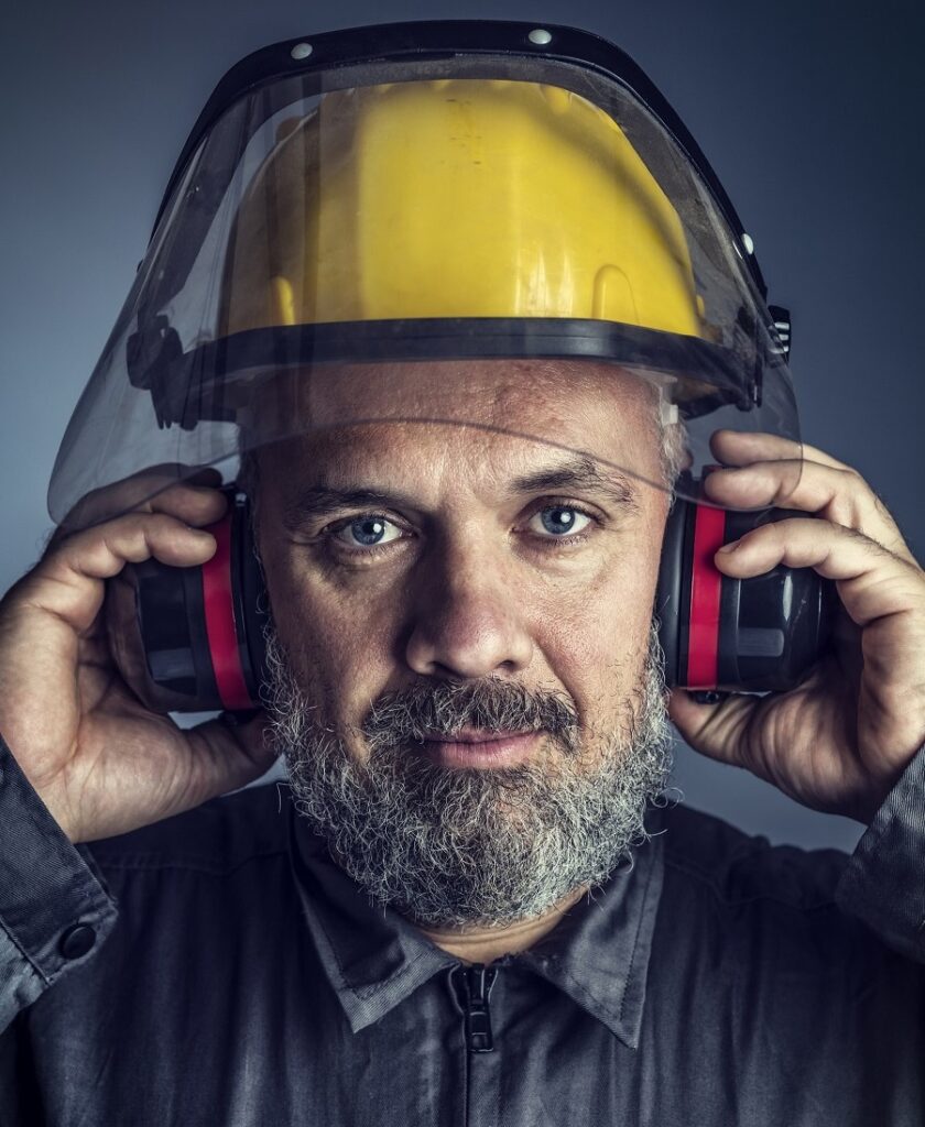 bearded man with yellow helmet holding ear protection