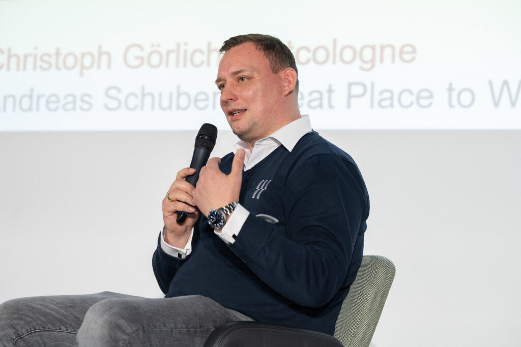 well dressed man sitting and speaking into a microphone to an audience