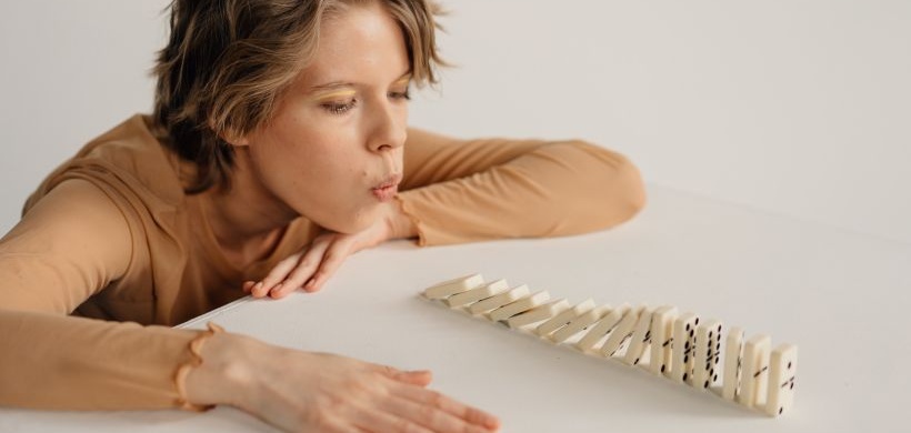 woman blowing down domino bricks on a white table